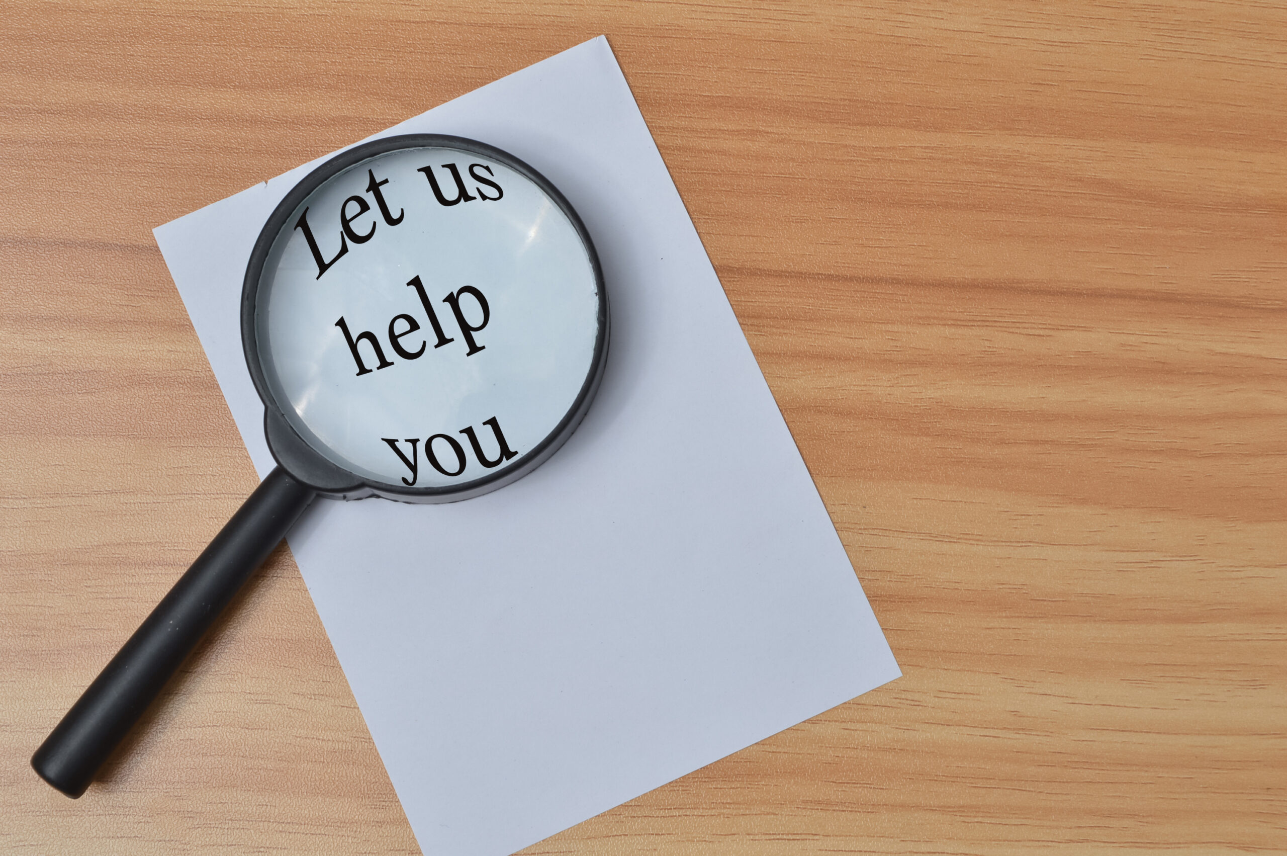 Top view of white paper and magnifying glass written with text LET US HELP YOU over wooden background. Business and education concept. Estudio Grafológico de Personajes